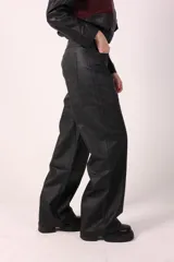 Pantalón de corte recto y holgado confeccionado en eco cuero con acabado texturizado. Presenta diseño de cinco bolsillos, cierre frontal y costuras reforzadas en los laterales.