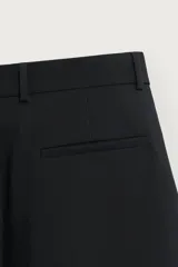Pantalón relaxed fit marrón oscuro, de corte ancho y recto, con pliegues frontales, bolsillos laterales y cierre con botón y cremallera.