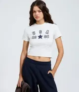 Remera baby look de algodón con cuello redondo y manga corta. Presenta un diseño ajustado al cuerpo y estampa frontal con la inscripción USA 2008 y una estrella central.