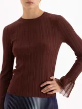 Top de tejido de punto fino color negro, con ajuste al cuerpo, cuello redondo y mangas largas que terminan en puños acampanados con detalle de tejido calado.