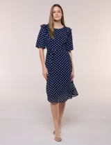 Vestido midi azul marino con estampado de lunares blancos, confeccionado en gasa semitraslúcida. Tiene escote redondo, mangas cortas acampanadas con volantes en los hombros, lazo ajustable en la cintura y falda con vuelo y forro interior.