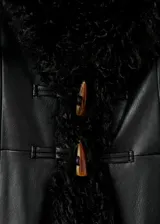 Abrigo largo de efecto piel con detalles de pelo sintético en cuello, puños y ruedo. Presenta diseño recto, cuello de pico, cierre frontal con botones y bolsillos laterales.