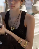 Collar con dije de forma irregular en tonos dorados y plateados, suspendido de un cordón doble de algodón negro.