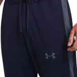 Conjunto deportivo Under Armour para hombre, compuesto por una campera con cierre frontal y cuello alto, y un pantalón de corte ajustado. Ambas piezas presentan el logo de la marca en color negro y franjas laterales oscuras.