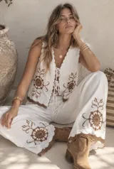 Conjunto de dos piezas compuesto por una musculosa y un short. La musculosa es sin mangas, con escote en V, cierre frontal con tiras para anudar y detalles bordados con diseño floral. El short cuenta con cintura elástica. Las terminaciones de la prenda presentan bordes scalloped (ondulados) con detalles bordados en contraste.