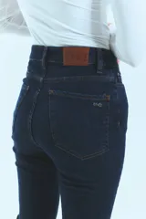 Pantalón de jean azul de tiro medio alto, corte oxford con botamanga ancha y tajo lateral. Cierre frontal con cinco botones metálicos.