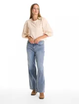 Blusa color beige con bordado floral al tono en el pecho y la espalda. Presenta mangas largas abullonadas con frunces en los hombros y puños festoneados. El ruedo cuenta con un acabado festoneado en ondas y la espalda incluye una abertura tipo gota con cierre de botón.