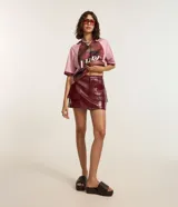 Short pollera de tiro medio confeccionado en poliuretano con acabado símil cuero. Presenta diseño de corte recto, cierre frontal con cremallera, trabillas para cinturón y dos bolsillos delanteros con solapa.