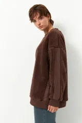 Buzo negro de tela tipo teddy, de manga larga y cuello redondo. Presenta recortes de nylon en mangas y laterales.