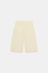 Bermudas de tiro medio color amarillo claro, confeccionadas en mezcla de algodón. Presentan cintura con trabillas, bolsillos laterales ocultos en costura, pliegues delanteros y cierre frontal con cremallera, botón y ganchos metálicos.