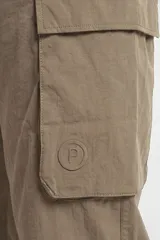 Pantalón cargo de nylon color beige, con elástico en la cintura y en los puños. Presenta bolsillos laterales con solapa y un logo de goma aplicado en uno de ellos.