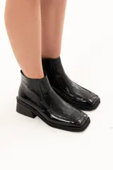 Bota corta de cuero negro con acabado brillante, diseño de punta cuadrada y taco bloque. Presenta cierre lateral interno y detalle de ribete en la capellada.