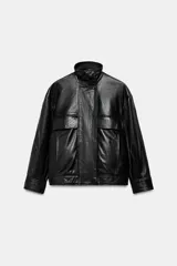 Chaqueta de piel negra con cuello alto, manga larga y cierre frontal con cremallera y botones a presión ocultos bajo solapa. Presenta bolsillos de plastrón con solapa en el frente y forro interior a tono.