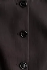 Chaleco sastrero de color marrón oscuro, con cuello redondo, cierre frontal con botones y diseño entallado.