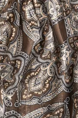 Blusa de tejido transparente con cuello elevado y botones forrados en la nuca. Presenta mangas largas con puños abotonados y un bajo levemente redondeado con estampado paisley.