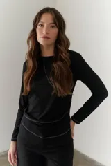Remera de manga larga color negro, confeccionada en algodón grueso. Presenta cuello redondo y detalles de costuras blancas en contraste que forman líneas geométricas en el frente y puños.