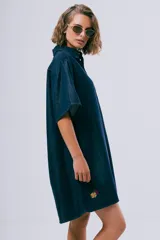 Vestido corto de denim azul oscuro, con cuello camisero, mangas cortas, cierre frontal con botones, bolsillo aplicado en el pecho y calce holgado.