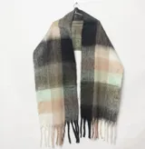 Bufanda mantón de tejido suave con diseño a cuadros en tonos verdes, negros, beige y blancos, terminada con flecos en los extremos.