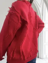 Sweater rojo de punto con cuello redondo y mangas largas. Presenta detalles de flecos en forma de rombos en el frente, la espalda y las mangas.