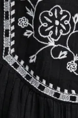 Pollera corta negra de tejido liviano con efecto arrugado y detalles bordados florales en blanco en los paneles laterales superiores. Presenta cintura clásica con cierre oculto y costura fruncida que genera vuelo en la parte inferior.