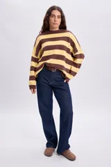Buzo tejido oversize de manga larga con diseño de rayas horizontales en color amarillo y marrón, cuello redondo y hombros caídos.