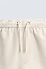 Short de baño de color beige con textura seersucker, cintura elástica con cordón ajustable, bolsillos laterales y forro interior.
