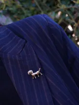 Pin metálico con forma de perro pequeño, diseñado para colocar en solapas, bolsos o abrigos.