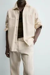 Pantalón chino de corte relajado, color beige claro, con textura de rayas verticales sutiles. Presenta cintura ajustable con cordón interior, bolsillos delanteros y bolsillos traseros de vivo.