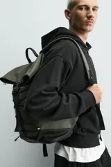 Mochila técnica de acabado engomado en color negro. Presenta un diseño de solapa con cierre de hebilla de liberación rápida y un sistema de cordones elásticos frontales. Incluye compartimento para dispositivos electrónicos, espalda acolchada y correas ajustables.