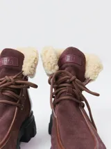 Borcegos de caña baja con diseño robusto, confeccionados en una combinación de gamuza y cuero sintético en tonos verde oliva. Presentan suela track de goma dentada en color suela, cordones al tono con ojalillos amarillos y cuello acolchado para mayor confort.