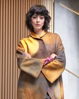 Tapado de lana merino afieltrada color ocre con teñido artesanal tie dye en forma de luna, cierre cruzado asimétrico con broches, cuello alto y bolsillos laterales.