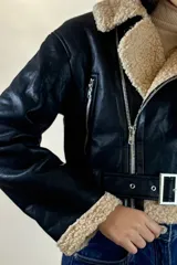 Campera tipo aviador de cuero sintético marrón con interior y detalles de corderito beige. Presenta cierre frontal cruzado, cuello solapa amplio, puños con corderito y cinturón ajustable en la cintura con hebilla metálica.