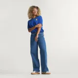 Pantalón Adidas Firebird de denim azul de corte holgado, con tiro medio y las icónicas tres tiras blancas a lo largo de los laterales de las piernas.