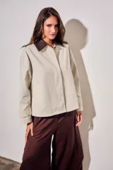 Trench corto de corte oversize con estampado de cuadros finos en tonos beige y verde. Presenta cuello camisero en contraste de color marrón oscuro, cierre frontal con botones y mangas largas con detalle de trabas en los puños.