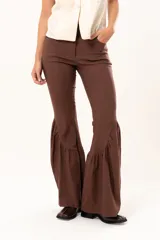 Pantalón de corte ajustado en la parte superior y pierna acampanada con volados en el ruedo. Presenta cierre frontal y bolsillos laterales.