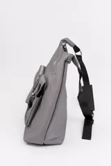 Cartera bandolera color gris de material sintético con correa ajustable negra y hebilla. Posee dos bolsillos frontales exteriores, uno con cierre y tirador largo y otro con solapa y hebilla decorativa.