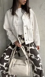 Sobrecamisa color crema con cuello camisero, cierre frontal con botones a presión, bolsillos de parche con solapa en el pecho y corte holgado.