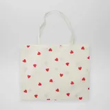 Tote bag de tela color crudo con estampado de corazones rojos.