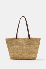 Bolso tipo shopper confeccionado en yute trenzado, con doble asa de mano en cuero sintético color marrón.