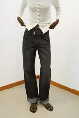 Jeans de tiro alto color negro lavado, con cintura cruzada, cinco bolsillos y pernera recta. El bajo está acabado en vuelta y tiene cierre frontal cruzado con cremallera y botones.