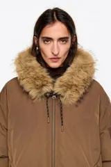 Campera tipo bomber acolchada en color marrón, con capucha con borde de piel sintética, cierre frontal con cremallera, puños y bajo de punto elástico, y aberturas laterales.