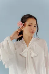 Blusa de algodón color blanco, con cuello alto y lazo frontal para atar. Presenta mangas largas con volados en los puños y un diseño holgado y romántico.