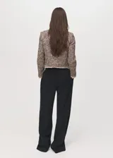Chaqueta de tweed con diseño recto y cuello redondo. Presenta cierre frontal con botones, manga larga y cuatro bolsillos de solapa en la parte delantera. Destaca por sus terminaciones deshilachadas y ribetes en contraste.