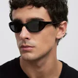 Lentes de sol con diseño cat-eye slim y envolvente, con montura y cristales en color negro.