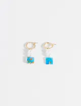 Par de aros dorados tipo argolla con dije colgante compuesto por dos perlas sintéticas y una pieza de vidrio cuadrada con diseño floral.