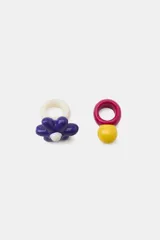 Pack de dos anillos de resina multicolor. Uno de los anillos presenta un diseño liso en color fucsia con una aplicación esférica amarilla en contraste, mientras que el otro cuenta con una base blanca y un aplique en relieve con forma de flor en tonos azul y blanco.
