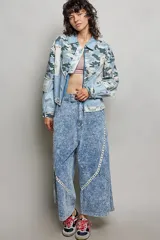 Chaqueta de denim de corte holgado y manga larga, con diseño en técnica de patchwork que combina sectores de mezclilla clásica, estampa de camuflaje, parches florales y detalles de encaje blanco. Cuenta con cierre frontal de cremallera metálica y cuello camisero.