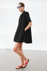 Vestido corto de algodón con cuello solapa, manga corta y cierre frontal con botones. Presenta un diseño evasé con bolsillos laterales ocultos en las costuras.