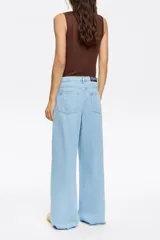 Pantalón largo de jean, color celeste claro, con corte wide leg y tiro bajo. Presenta cierre frontal con botón, cinco bolsillos y cordón ajustable en la cintura.