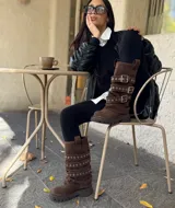 Botas de caña media color marrón, confeccionadas en gamuza, con suela trackera y múltiples correas horizontales con hebillas metálicas y ojales decorativos.
